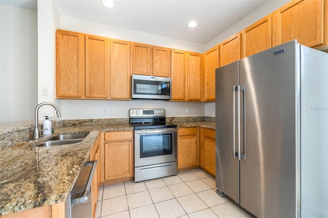 kitchen with sink, a textured ceiling, dark stone countertops, light tile patterned floors, and stainless steel appliances