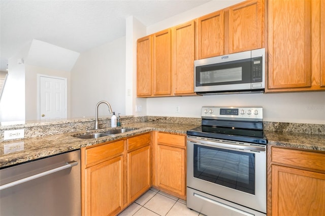 kitchen with appliances with stainless steel finishes, sink, dark stone countertops, light tile patterned floors, and kitchen peninsula