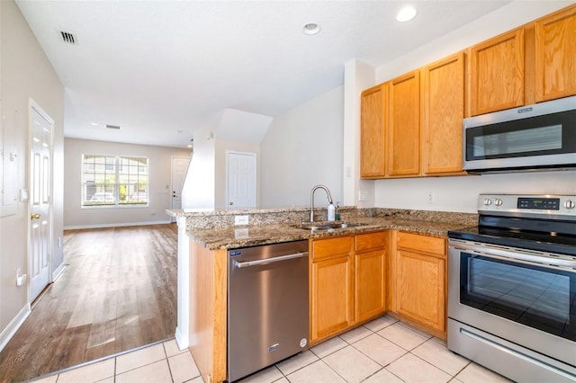 kitchen featuring stone counters, appliances with stainless steel finishes, sink, light tile patterned floors, and kitchen peninsula