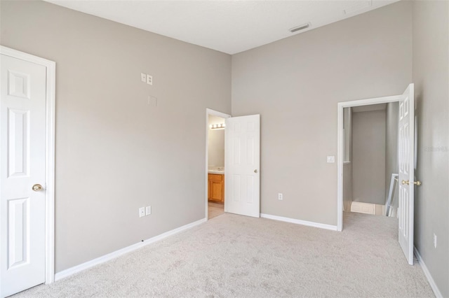 unfurnished bedroom with a high ceiling, ensuite bathroom, and light carpet