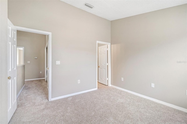 unfurnished room featuring a towering ceiling, light colored carpet, and a textured ceiling