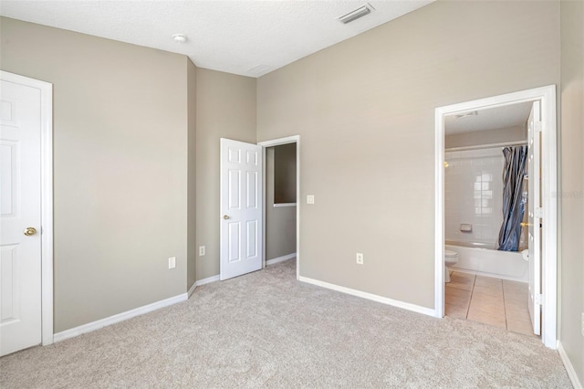 unfurnished bedroom featuring light colored carpet, a textured ceiling, and ensuite bath