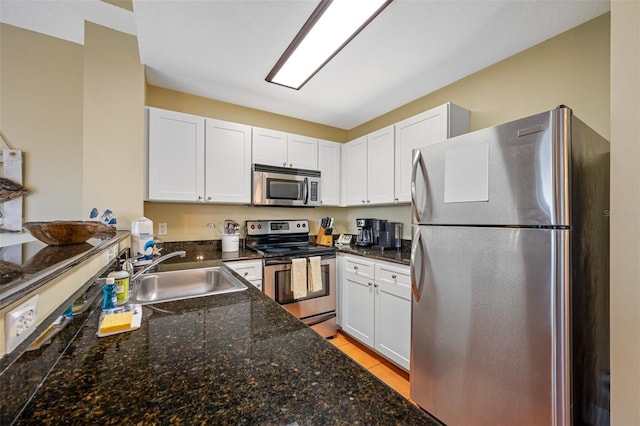 kitchen with dark stone countertops, stainless steel appliances, sink, and white cabinets