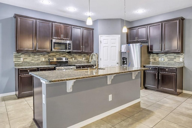 kitchen featuring sink, a breakfast bar area, decorative light fixtures, appliances with stainless steel finishes, and an island with sink