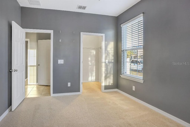 unfurnished bedroom featuring a walk in closet, light colored carpet, and a closet