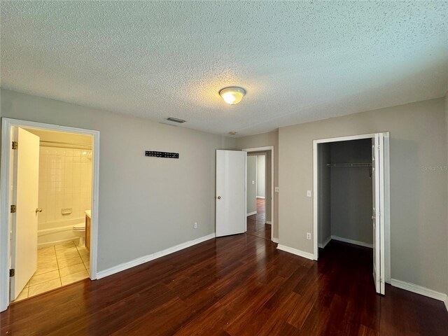 unfurnished bedroom with ensuite bathroom, a textured ceiling, dark hardwood / wood-style flooring, and a closet