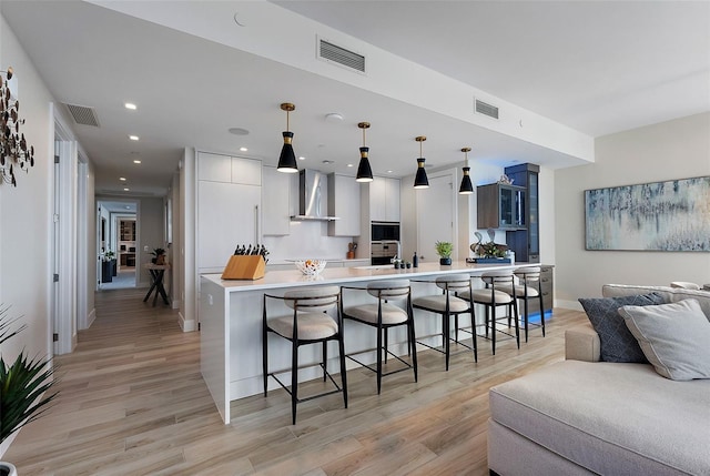 kitchen featuring a breakfast bar, hanging light fixtures, kitchen peninsula, light wood-type flooring, and wall chimney exhaust hood