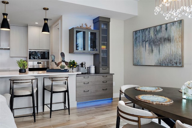 kitchen featuring pendant lighting, light wood-type flooring, a breakfast bar area, and gray cabinetry