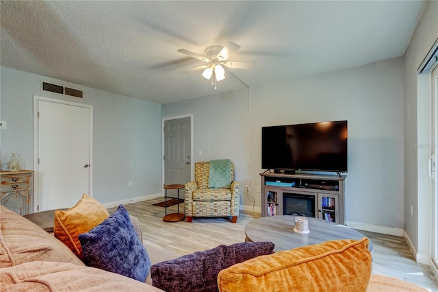 living room featuring ceiling fan, a textured ceiling, and light wood-type flooring