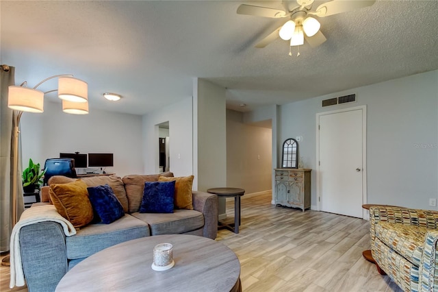 living room with ceiling fan, a textured ceiling, and light hardwood / wood-style floors