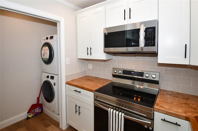 kitchen featuring white cabinetry, butcher block countertops, stacked washer and dryer, and appliances with stainless steel finishes