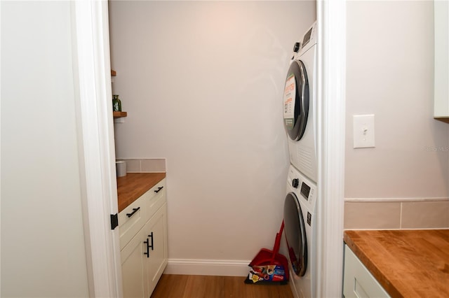 clothes washing area with stacked washer and dryer, light wood-type flooring, and cabinets