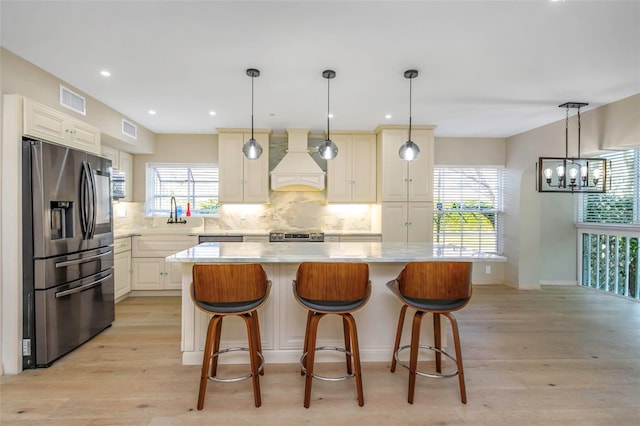 kitchen with light hardwood / wood-style flooring, appliances with stainless steel finishes, backsplash, a kitchen island, and custom exhaust hood