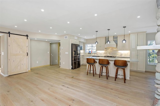 kitchen with a barn door, light hardwood / wood-style flooring, custom range hood, pendant lighting, and a large island