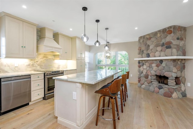 kitchen featuring premium range hood, a center island, pendant lighting, stainless steel appliances, and cream cabinets