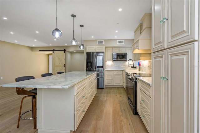 kitchen featuring appliances with stainless steel finishes, a breakfast bar, a large island, light stone counters, and a barn door