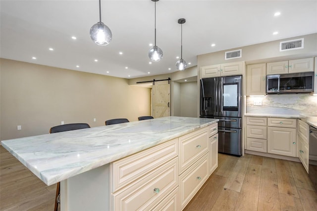 kitchen with a kitchen bar, light stone counters, a center island, appliances with stainless steel finishes, and a barn door