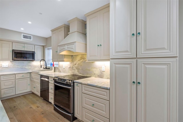 kitchen with sink, light wood-type flooring, appliances with stainless steel finishes, custom range hood, and backsplash