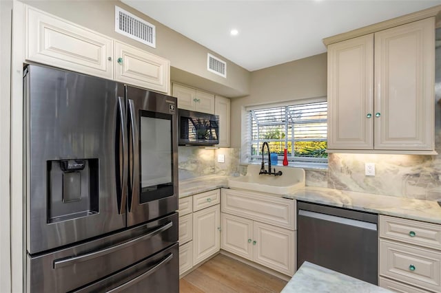 kitchen with appliances with stainless steel finishes, sink, backsplash, light stone countertops, and light wood-type flooring