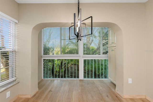 unfurnished dining area with light wood-type flooring, a wealth of natural light, and an inviting chandelier