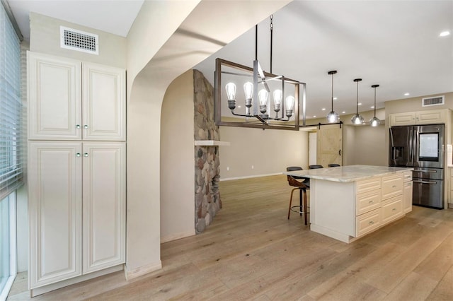 kitchen featuring decorative light fixtures, a center island, stainless steel fridge, a barn door, and light stone countertops