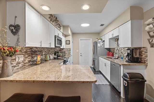 kitchen with a breakfast bar area, appliances with stainless steel finishes, white cabinetry, light stone countertops, and kitchen peninsula