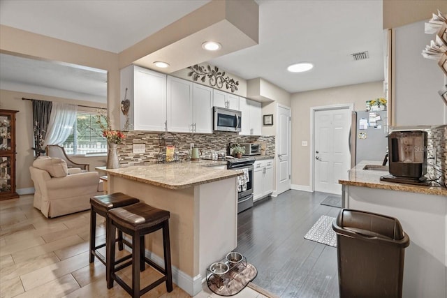 kitchen with light stone counters, appliances with stainless steel finishes, backsplash, and white cabinets