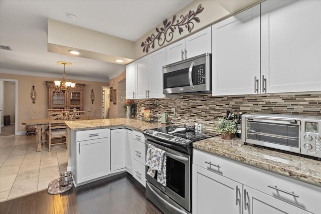 kitchen with appliances with stainless steel finishes, decorative light fixtures, white cabinetry, decorative backsplash, and kitchen peninsula