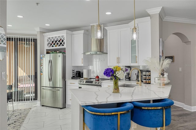 kitchen featuring arched walkways, a sink, appliances with stainless steel finishes, crown molding, and wall chimney range hood