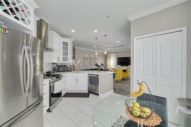 kitchen with a peninsula, a sink, appliances with stainless steel finishes, crown molding, and wall chimney range hood