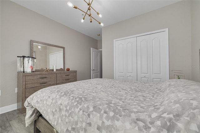 bedroom featuring a closet, a chandelier, baseboards, and wood finished floors