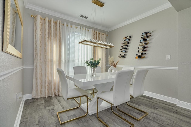 dining area featuring visible vents, ornamental molding, wood finished floors, baseboards, and a textured wall