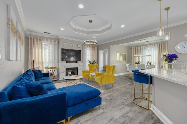 living area with a premium fireplace, a tray ceiling, recessed lighting, light wood-style floors, and crown molding