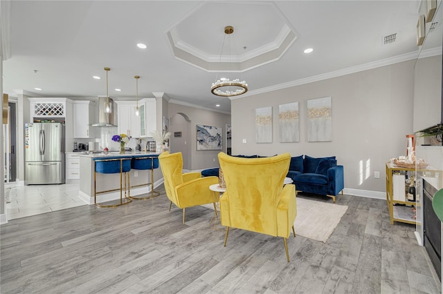 living room with visible vents, a tray ceiling, recessed lighting, light wood-style floors, and crown molding