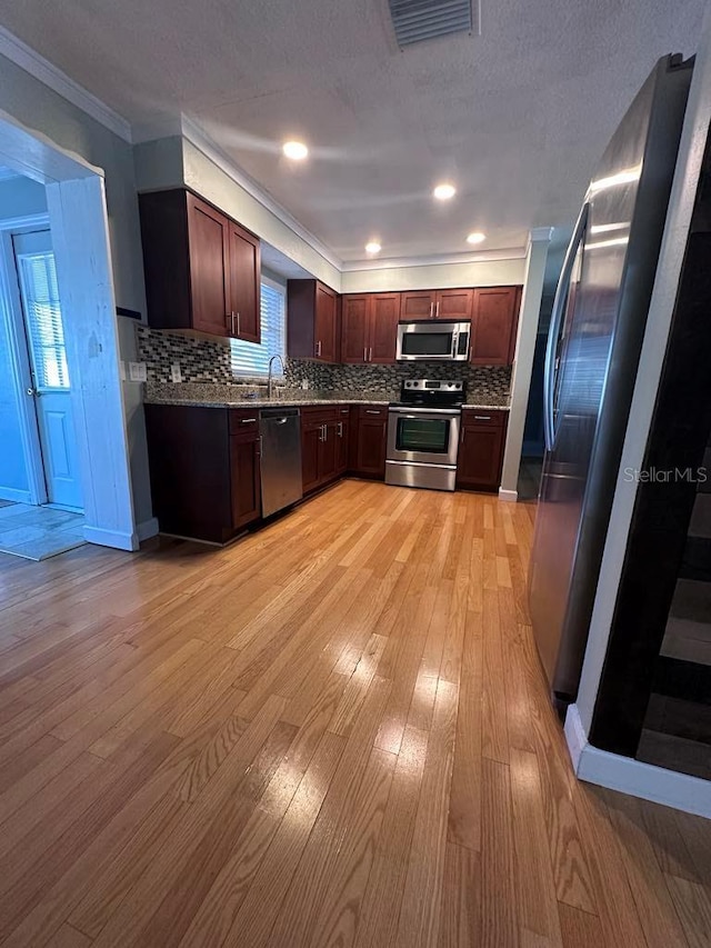 kitchen featuring backsplash, ornamental molding, stainless steel appliances, and light wood-type flooring