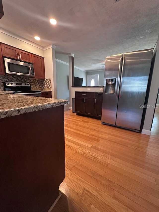 kitchen featuring dark brown cabinets, stainless steel appliances, ornamental molding, decorative backsplash, and light wood-type flooring