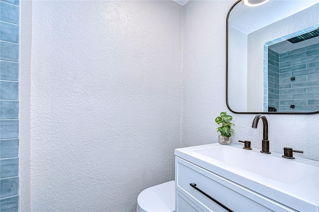 bathroom with toilet, vanity, and a textured wall