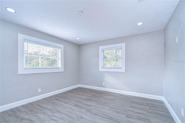 spare room featuring recessed lighting, plenty of natural light, wood finished floors, and baseboards