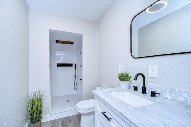 full bathroom with wood finished floors, a textured wall, toilet, vanity, and a walk in shower