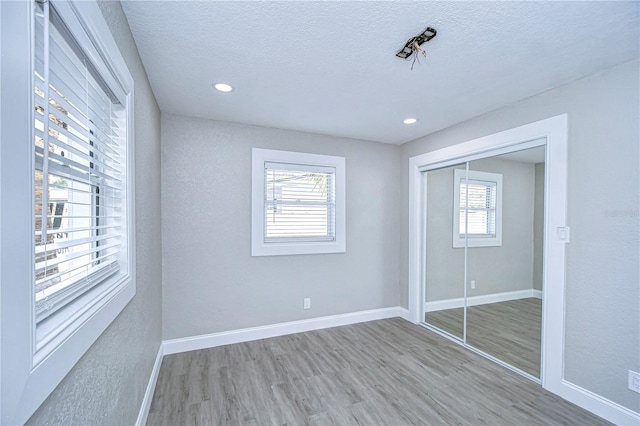 unfurnished bedroom featuring a textured ceiling, recessed lighting, wood finished floors, baseboards, and a closet