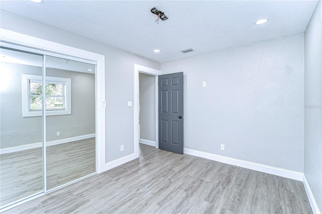 unfurnished bedroom featuring a textured ceiling, a closet, wood finished floors, and baseboards