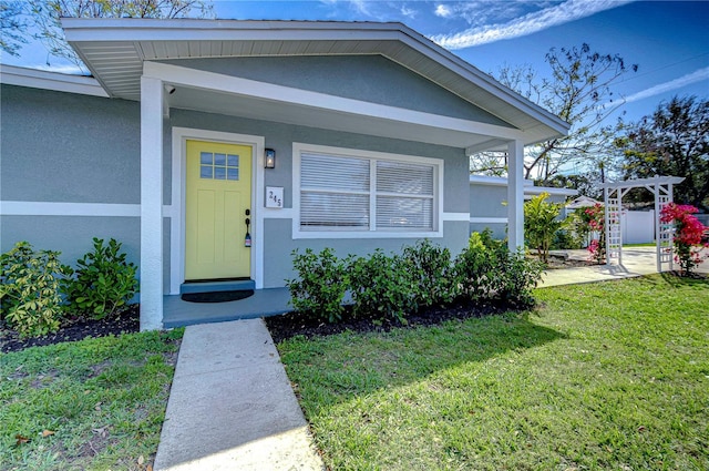 view of exterior entry with a yard, a pergola, and stucco siding