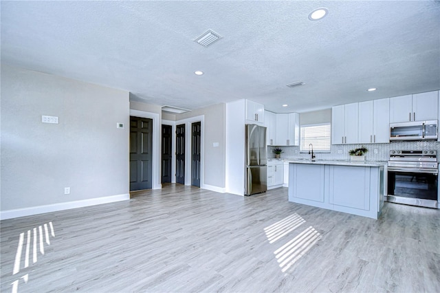 kitchen featuring light wood-type flooring, stainless steel appliances, light countertops, and open floor plan