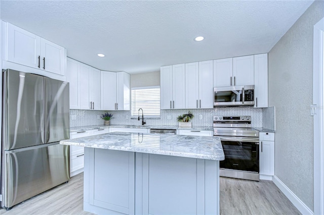 kitchen featuring appliances with stainless steel finishes, light wood-style floors, a textured wall, and backsplash