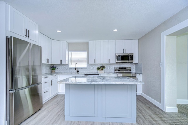 kitchen featuring stainless steel appliances, a sink, a center island, white cabinets, and decorative backsplash