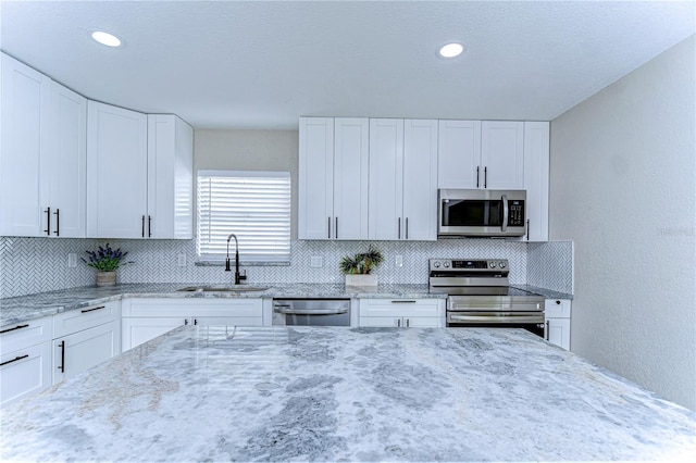 kitchen featuring light stone counters, a sink, white cabinetry, appliances with stainless steel finishes, and decorative backsplash