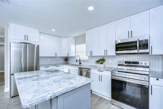 kitchen with a kitchen island, light stone countertops, stainless steel appliances, white cabinetry, and a sink