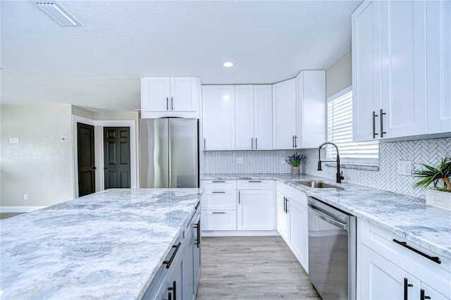 kitchen with light stone counters, stainless steel appliances, a sink, visible vents, and white cabinets