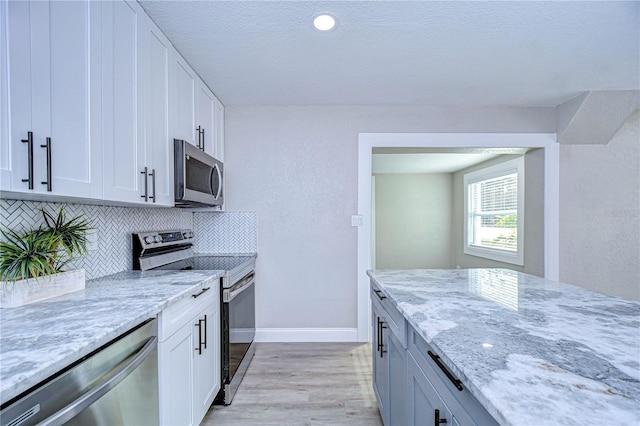 kitchen featuring white cabinets, light wood-style floors, appliances with stainless steel finishes, light stone countertops, and tasteful backsplash