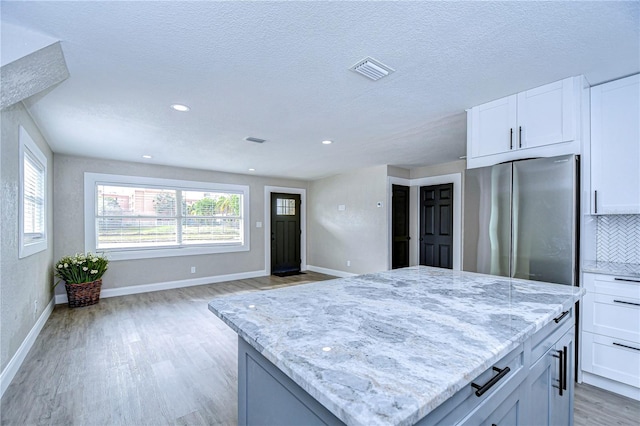 kitchen featuring light stone counters, visible vents, light wood-style floors, freestanding refrigerator, and tasteful backsplash